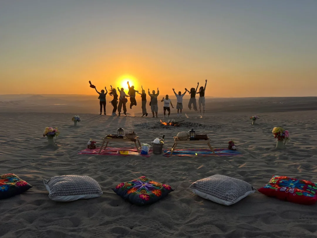 Travelers celebrating at sunset during the Exclusive Desert Campfire Experience in Huacachina Peru