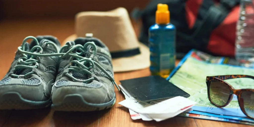 Travel essentials for a Machu Picchu trip including hiking shoes, passport, map, hat, water bottle and sunglasses